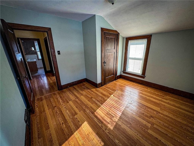 empty room featuring baseboards, wood finished floors, and vaulted ceiling