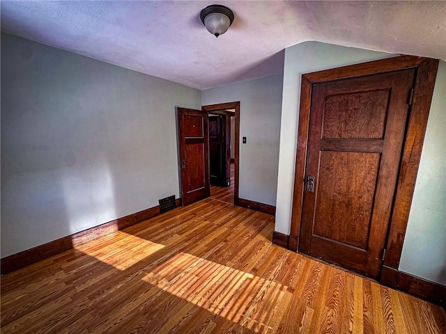 unfurnished bedroom featuring lofted ceiling, wood finished floors, and baseboards