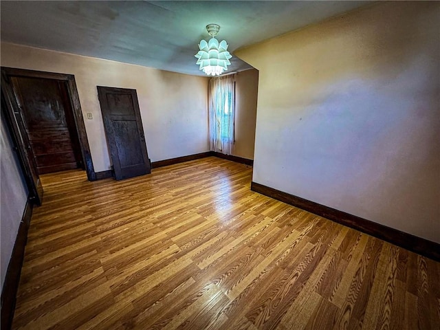 unfurnished room with an inviting chandelier, baseboards, and wood finished floors