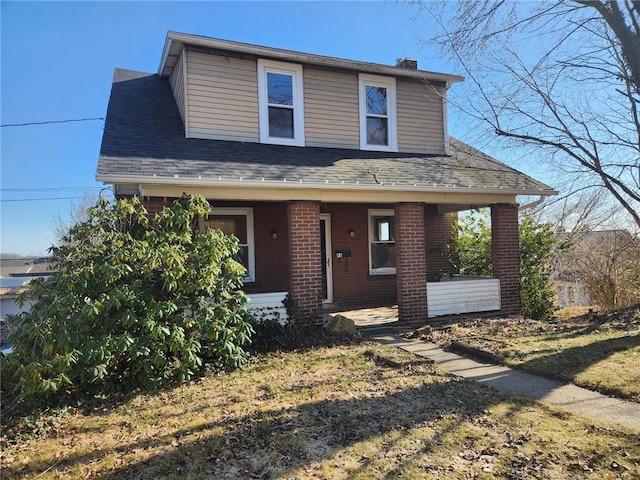 view of front facade featuring a porch, brick siding, roof with shingles, and a chimney