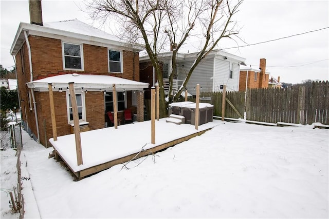 snow covered rear of property featuring a hot tub