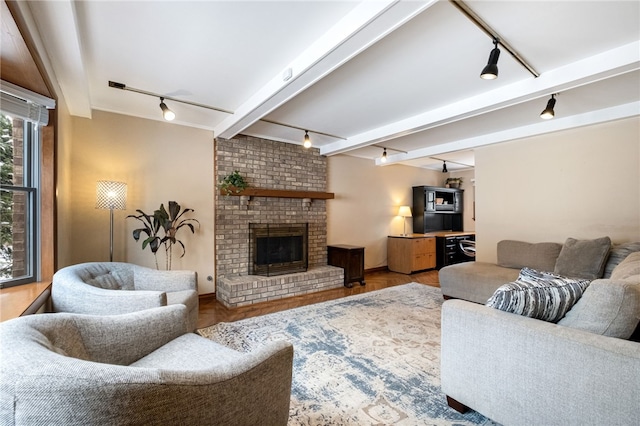 living room featuring hardwood / wood-style flooring, beam ceiling, rail lighting, and a brick fireplace