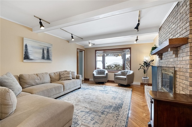 living room with light parquet floors, track lighting, a brick fireplace, and beam ceiling