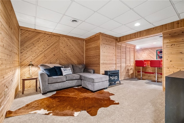 carpeted living room with a paneled ceiling, a wood stove, and wooden walls