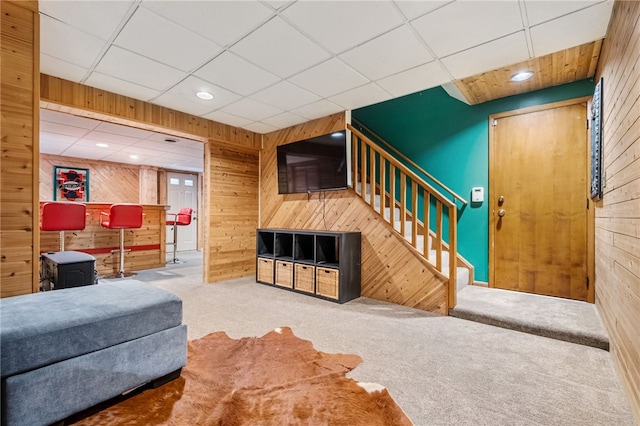 living room with a paneled ceiling, wooden walls, and carpet floors