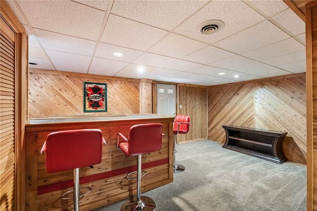 bar featuring a paneled ceiling, wood walls, and carpet