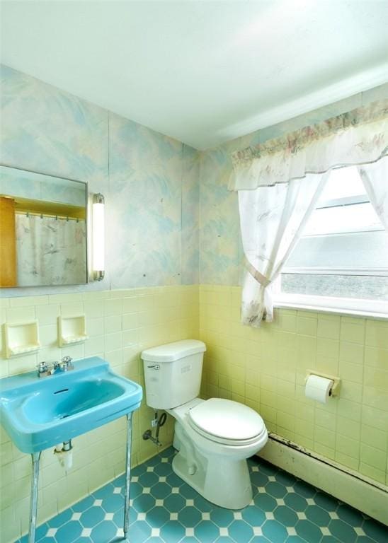 bathroom with a baseboard radiator, tile walls, toilet, and sink