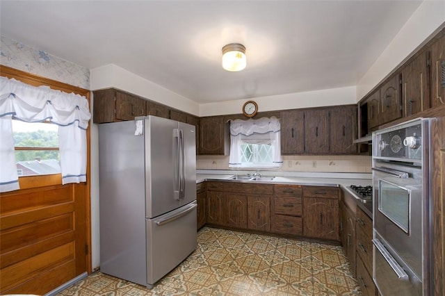 kitchen with a wealth of natural light, stainless steel appliances, dark brown cabinets, and sink