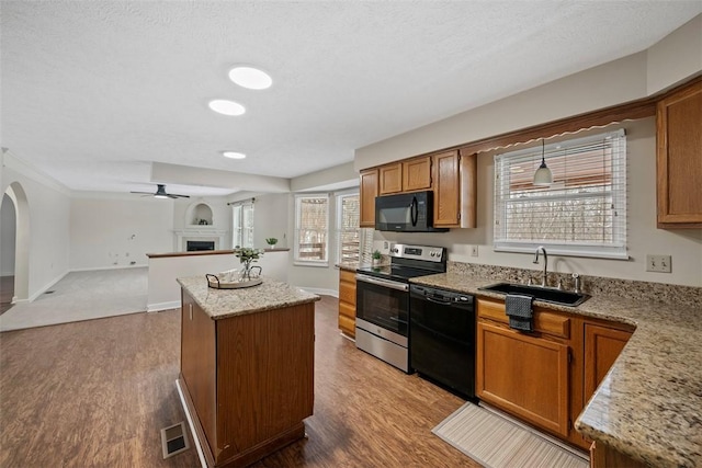 kitchen featuring light stone countertops, ceiling fan, sink, a center island, and black appliances