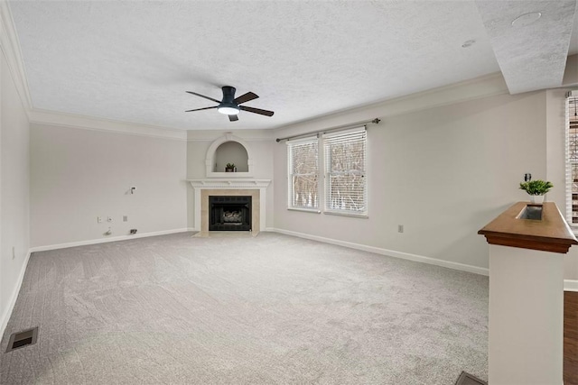 unfurnished living room featuring ceiling fan, carpet floors, a textured ceiling, a fireplace, and ornamental molding