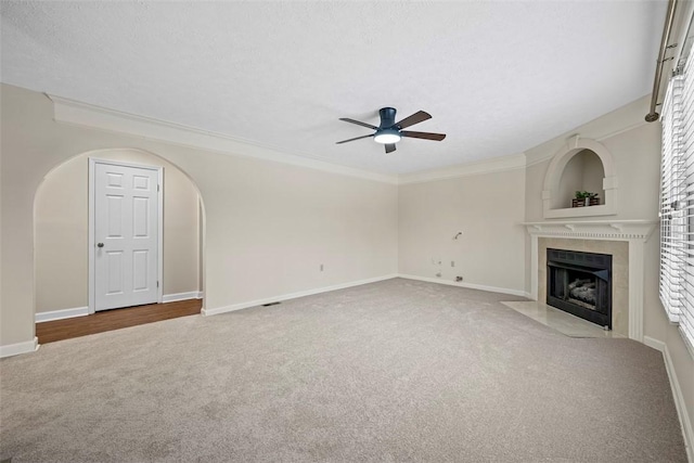 unfurnished living room with a tile fireplace, crown molding, ceiling fan, a textured ceiling, and carpet floors