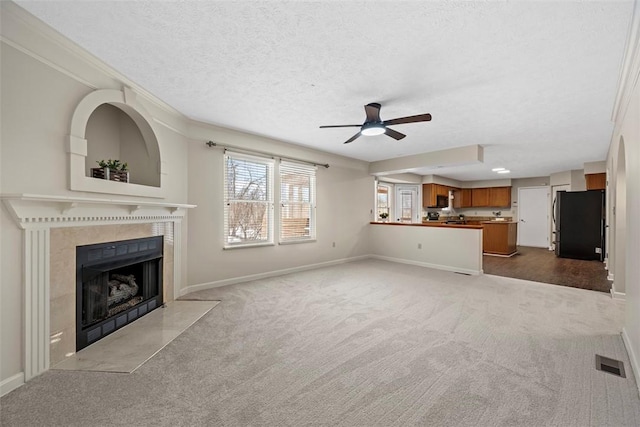 unfurnished living room featuring a tile fireplace, crown molding, ceiling fan, a textured ceiling, and light colored carpet