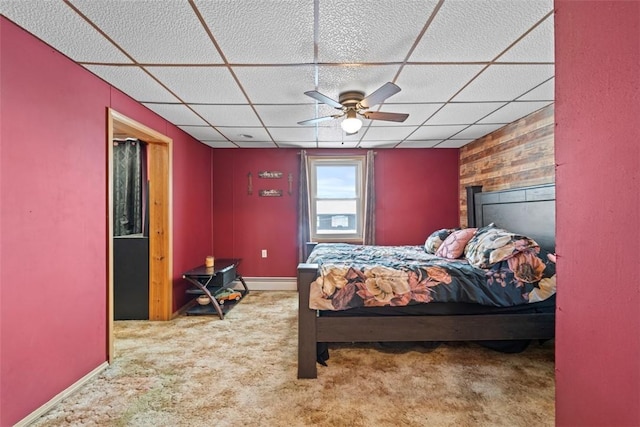 carpeted bedroom featuring baseboard heating, a paneled ceiling, ceiling fan, and wood walls