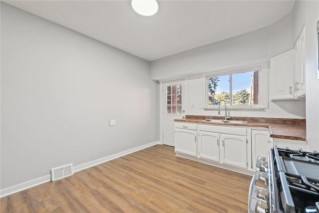 kitchen with wood counters, sink, light hardwood / wood-style floors, white cabinetry, and gas stove