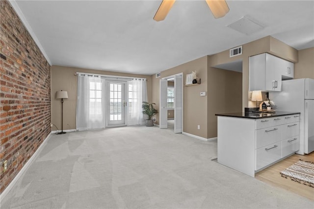 unfurnished living room featuring ceiling fan, light carpet, and brick wall