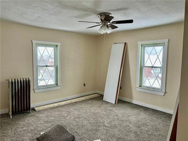 unfurnished room featuring carpet flooring, radiator, ceiling fan, and plenty of natural light