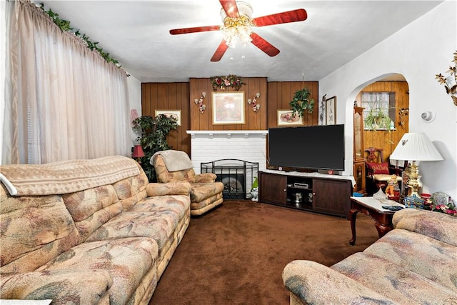 living room featuring dark colored carpet, a fireplace, wood walls, and ceiling fan