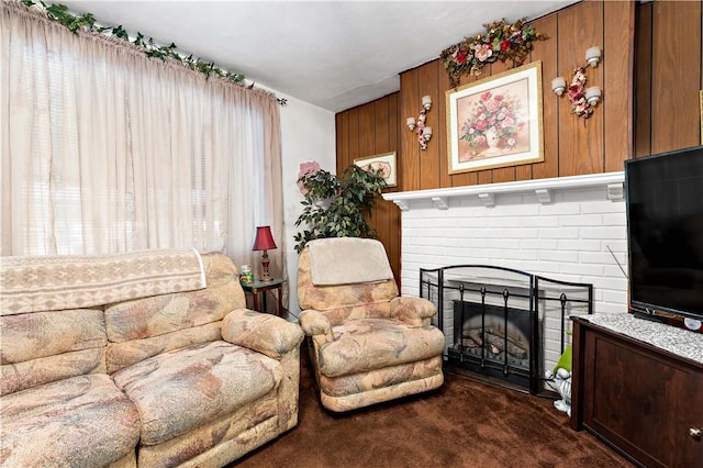 living room featuring a brick fireplace, wood walls, and dark carpet