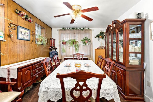 dining space with ceiling fan and wood walls