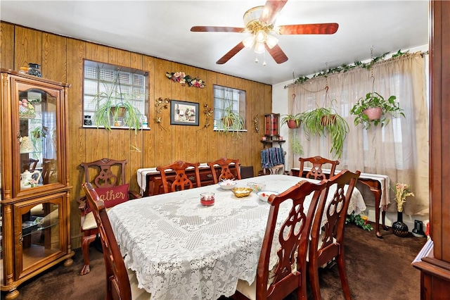 carpeted dining area with ceiling fan and wood walls