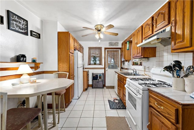 kitchen with ceiling fan, sink, white appliances, tile counters, and light tile patterned floors