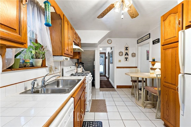 kitchen featuring ceiling fan, sink, white appliances, light tile patterned flooring, and tile counters