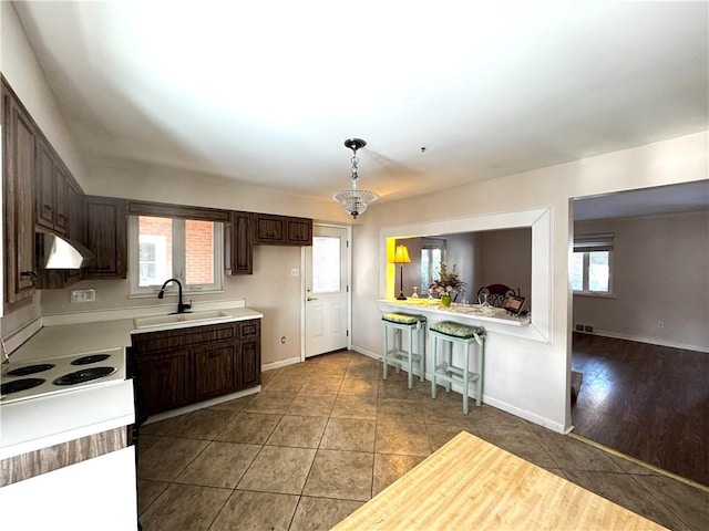 kitchen featuring dark brown cabinetry, sink, hanging light fixtures, and light tile patterned floors