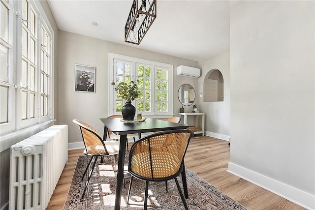 dining room featuring a wall mounted air conditioner, radiator heating unit, and light hardwood / wood-style floors