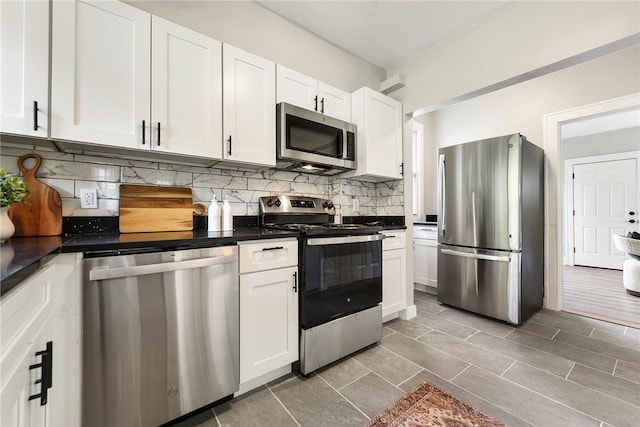 kitchen featuring white cabinets, dark tile patterned floors, stainless steel appliances, and tasteful backsplash