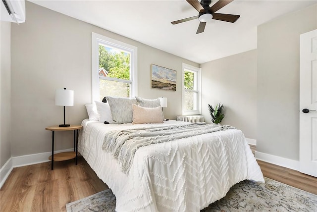 bedroom with ceiling fan, radiator heating unit, and wood-type flooring