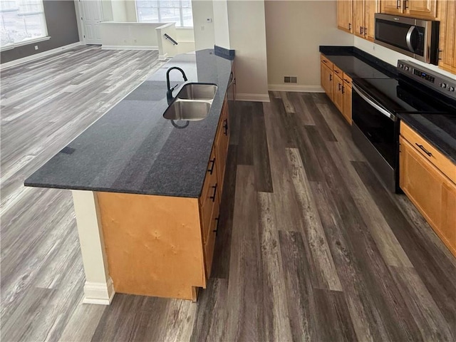 kitchen featuring sink, dark wood-type flooring, black electric range oven, dark stone counters, and a kitchen island with sink