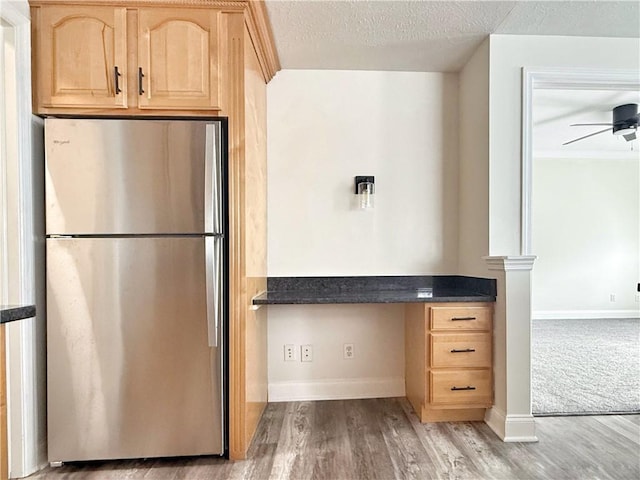 kitchen featuring light brown cabinets, light wood-type flooring, built in desk, a textured ceiling, and stainless steel refrigerator