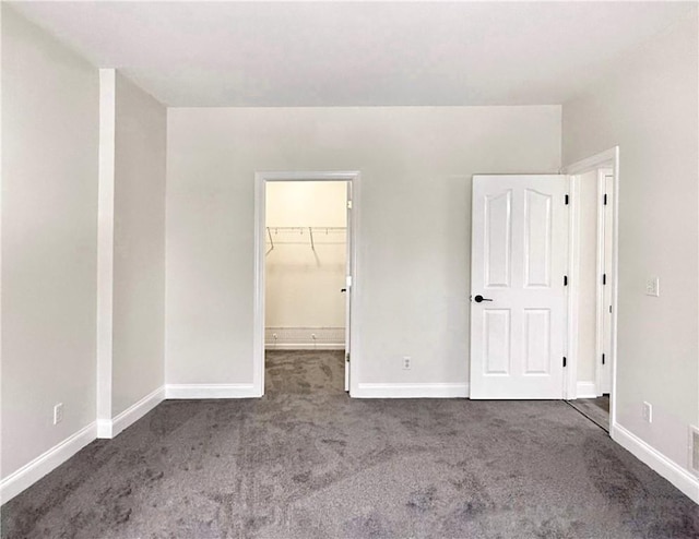 unfurnished bedroom featuring a spacious closet, a closet, and dark colored carpet