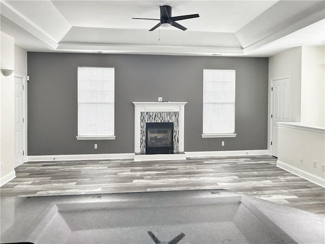 unfurnished living room with a raised ceiling, a wealth of natural light, ceiling fan, and hardwood / wood-style floors