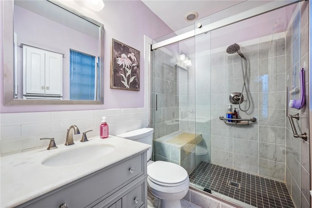 bathroom featuring vanity, toilet, a shower with shower door, and tile walls