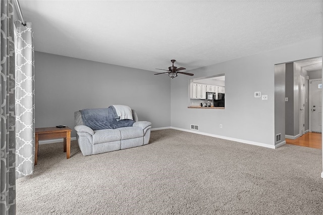 carpeted living room featuring ceiling fan, a stone fireplace, and a textured ceiling