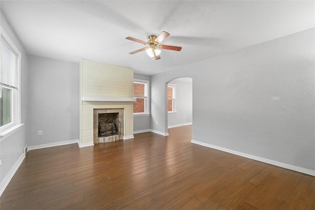 unfurnished living room with dark hardwood / wood-style floors, ceiling fan, a fireplace, and a wealth of natural light