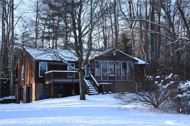 snow covered house featuring a garage and a sunroom