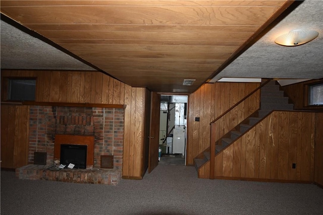 unfurnished living room with carpet flooring, a brick fireplace, wooden ceiling, and wood walls