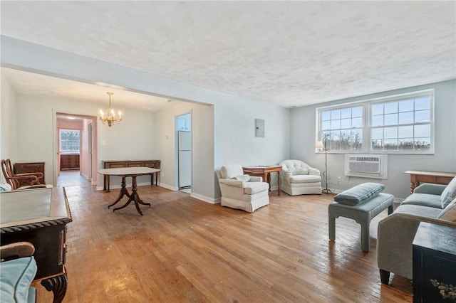 living room with a wall unit AC, an inviting chandelier, a textured ceiling, and light wood-type flooring