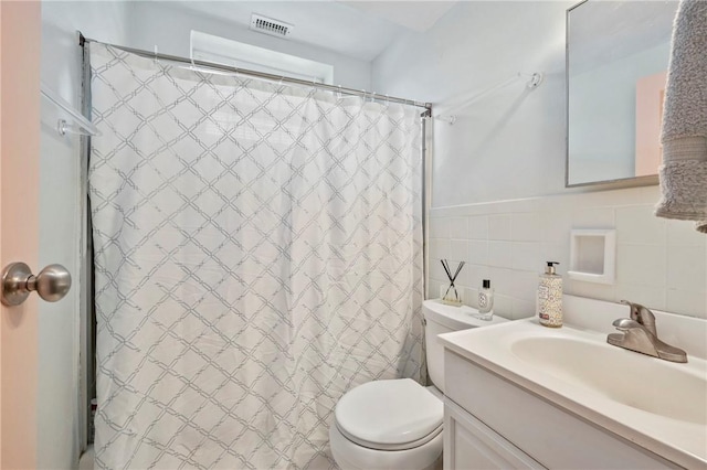 bathroom featuring walk in shower, vanity, toilet, and tile walls