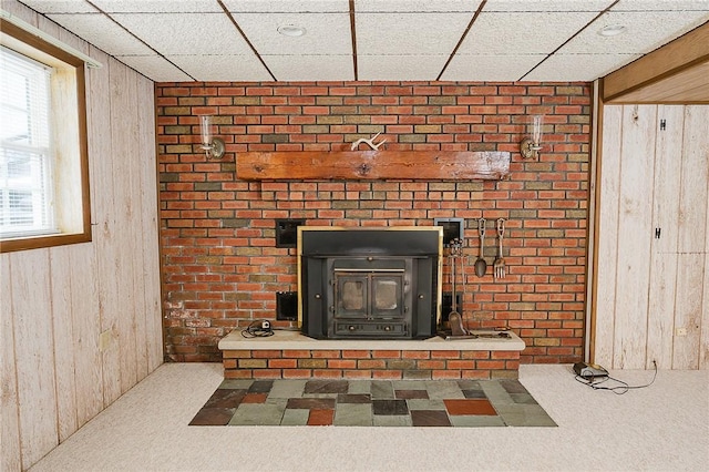 interior details with a paneled ceiling, carpet floors, a wood stove, and wooden walls