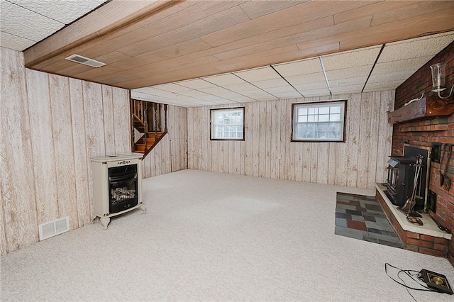 basement with carpet floors, a wood stove, and wooden walls