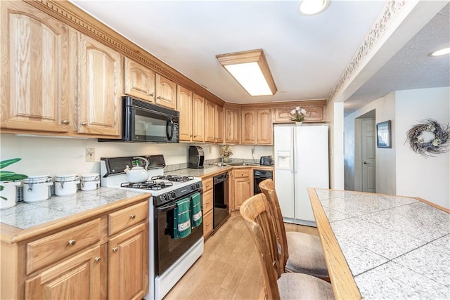 kitchen with black appliances, light hardwood / wood-style flooring, and tile countertops