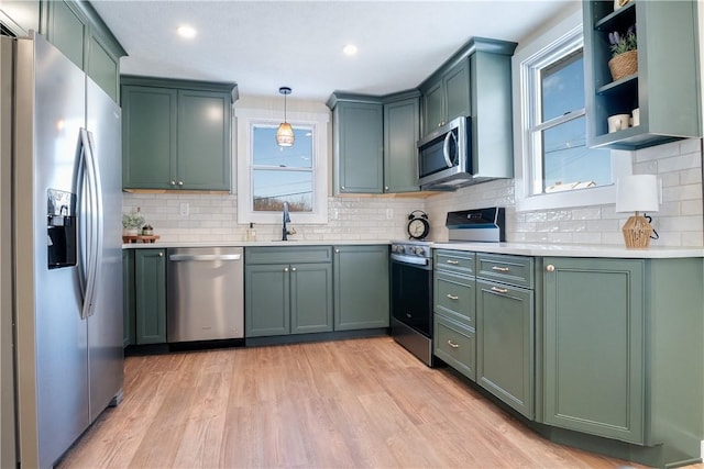 kitchen with backsplash, green cabinetry, light wood-type flooring, appliances with stainless steel finishes, and decorative light fixtures