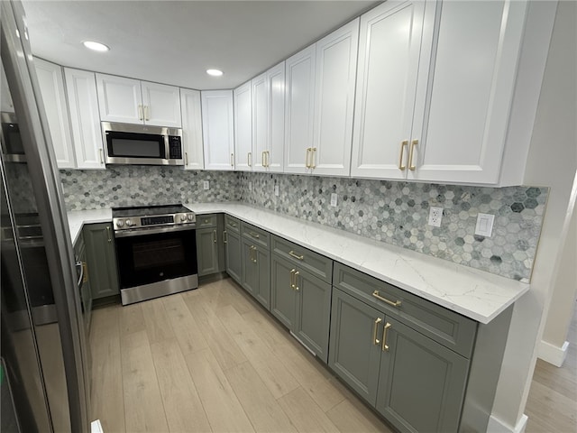 kitchen with light stone countertops, backsplash, gray cabinetry, stainless steel appliances, and white cabinetry