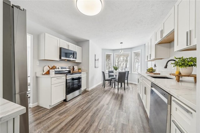 kitchen with white cabinets, hanging light fixtures, sink, appliances with stainless steel finishes, and wood-type flooring