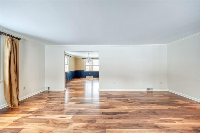 spare room with an inviting chandelier, ornamental molding, and light hardwood / wood-style flooring