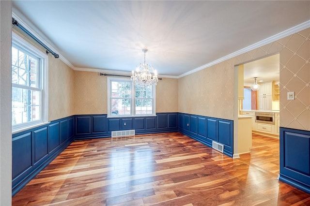 unfurnished dining area featuring hardwood / wood-style flooring, a notable chandelier, and ornamental molding