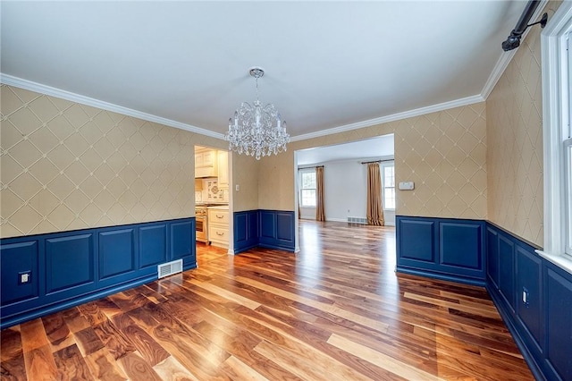 unfurnished dining area with hardwood / wood-style floors, crown molding, and a notable chandelier